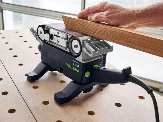 Festool BS 75 E-Plus Bandschleifer beim Schleifen einer Holzplatte, schwarzer Motor mit grünem Logo sichtbar
